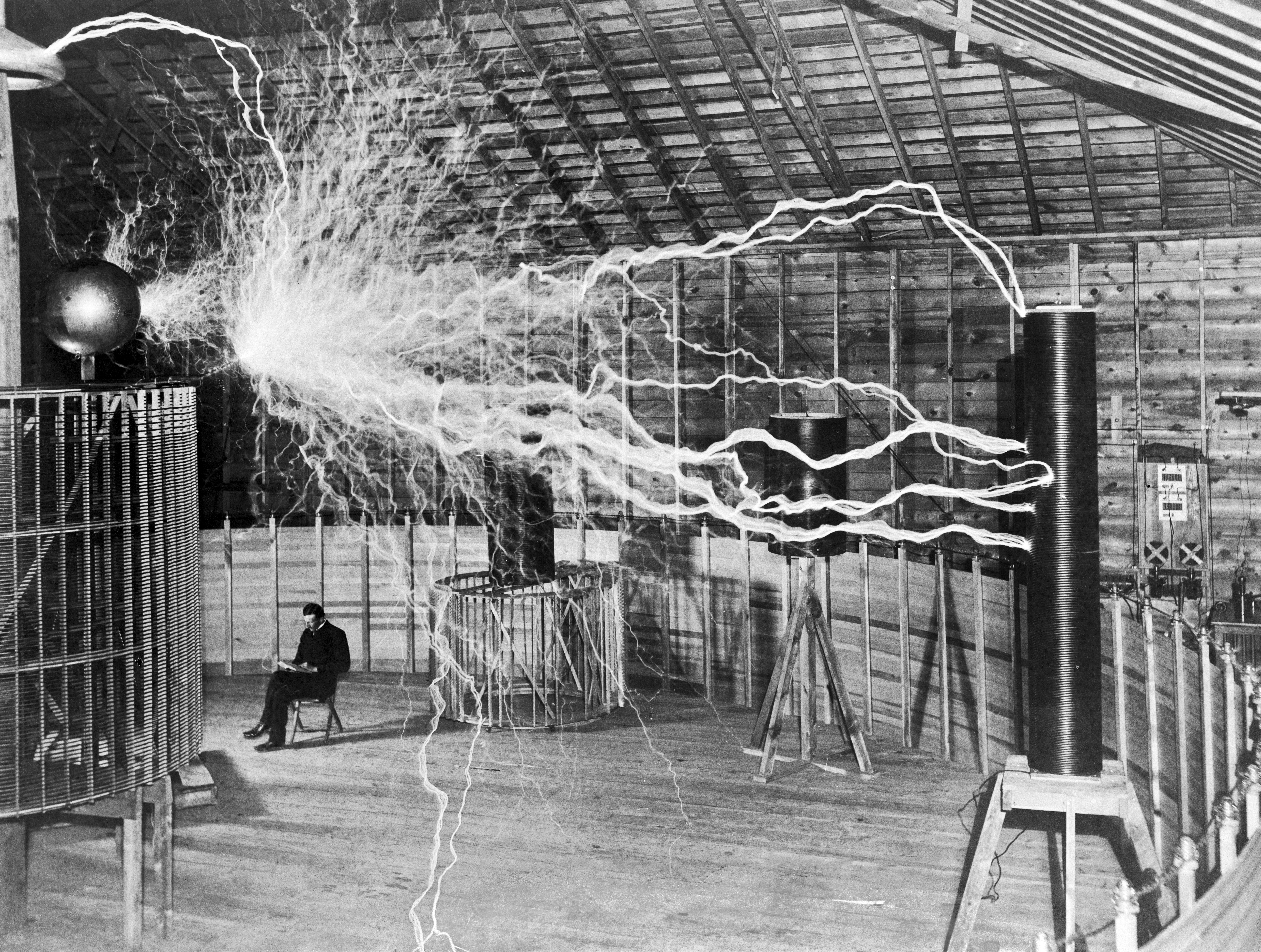 Tesla seated reading among large coil equipment, Colorado Springs.