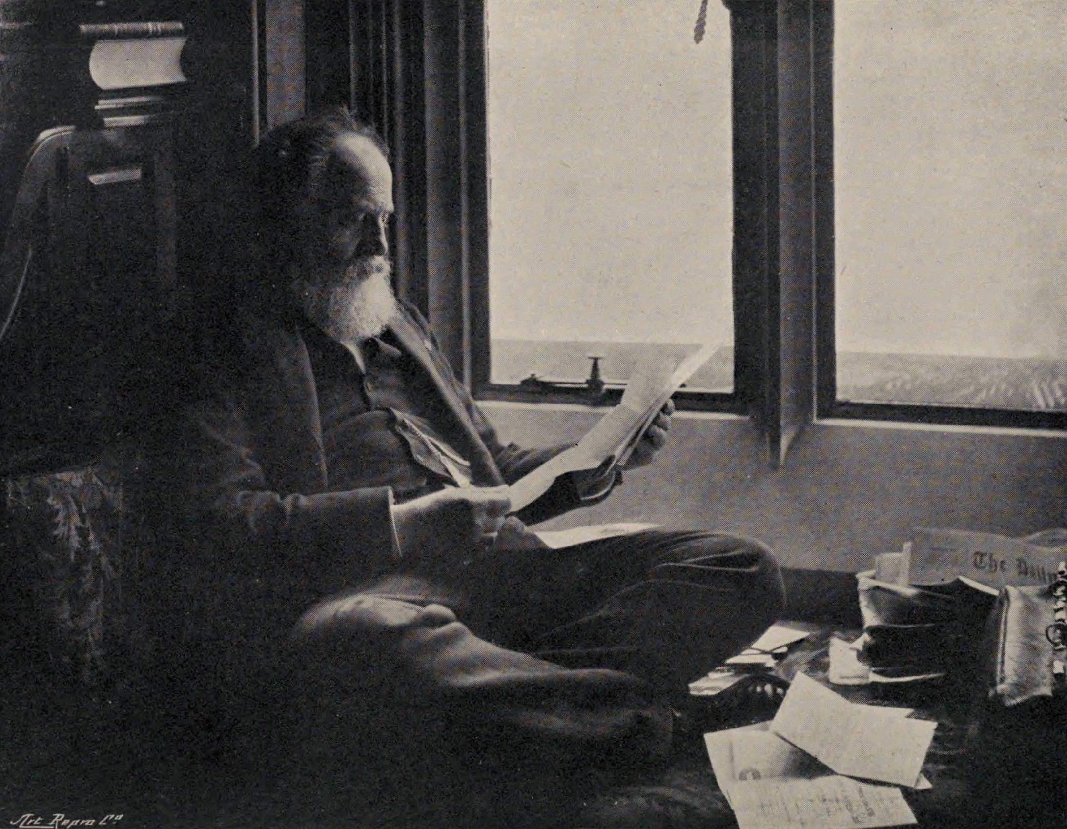 W. T. Stead reading correspondence at his desk in his last decade, with the day's newspapers piled at his side.