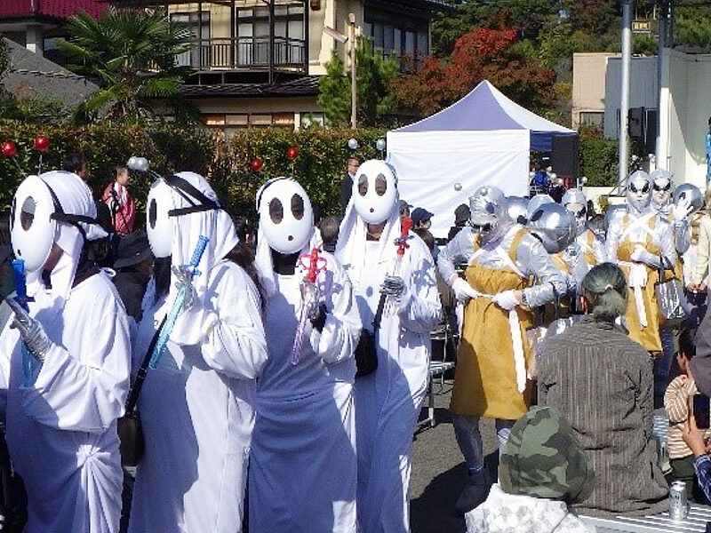 Festival-goers in white alien costumes with large black oval eyes march through the streets of Iino-machi during the 2023 UFO Festival