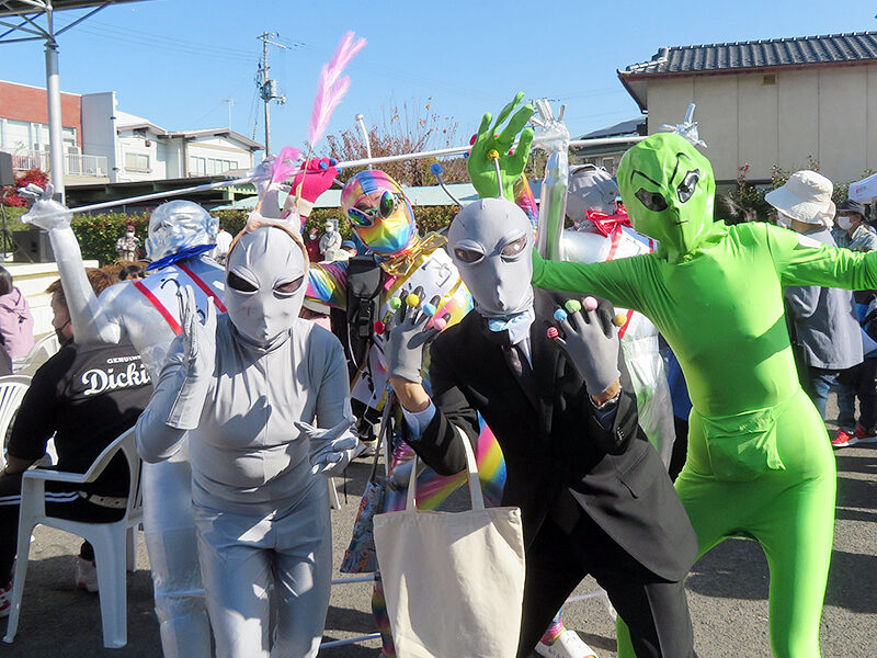 A group of costumed participants at the 2023 Iino UFO Festival pose together in silver, green, and holographic alien outfits