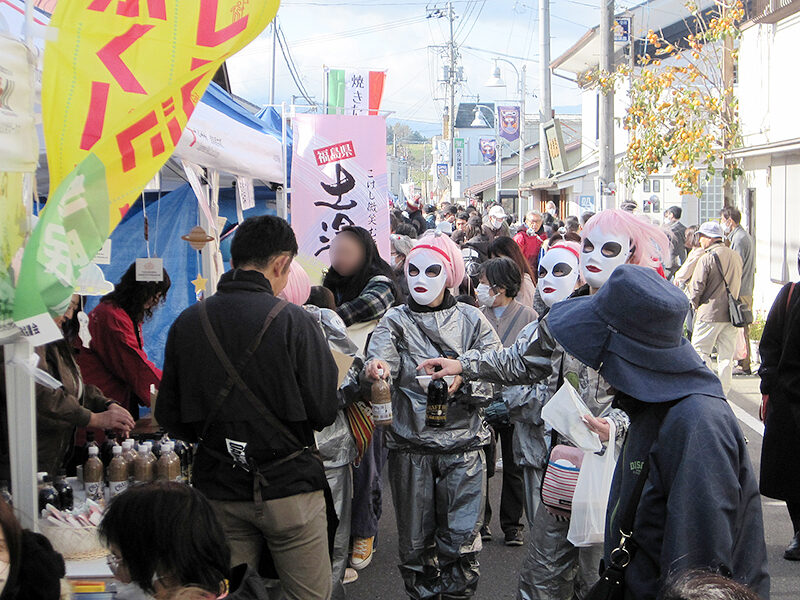 Crowds fill the streets of Iino-machi during the 2023 UFO Festival, with food stalls, banners, and costumed attendees visible along the shopping street