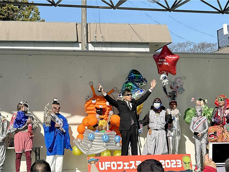 The main stage at the 2023 Iino UFO Festival, with costumed participants lined up during the Alien Costume Contest beneath a banner reading UFO Festival 2023